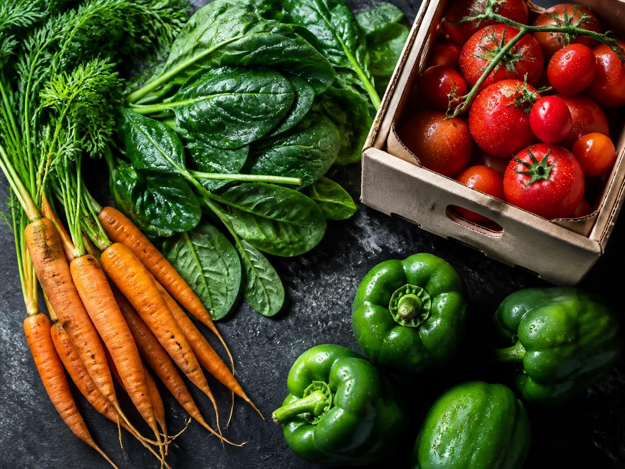 Freshly harvested carrots, spinach, tomatoes and peppers on a dark slate surface